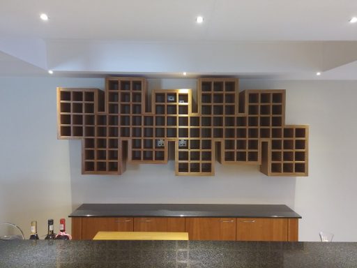 Wooden wine rack mounted on a wall, featuring multiple square compartments.